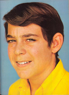 A young man with brown hair and wearing a yellow shirt.