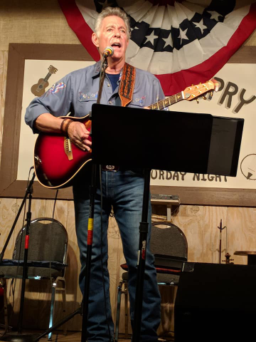 A man with a guitar and microphone in front of an american flag.