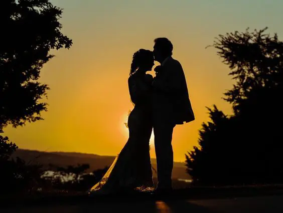 A couple is kissing in front of the sunset.