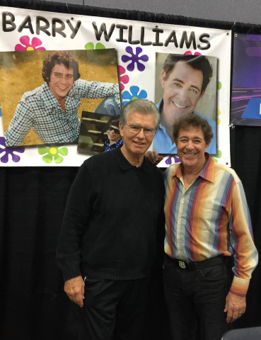 Two men posing for a picture in front of a poster.